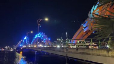 Da Nang Dragon Köprüsü 'nün parlak ışıklarıyla büyülü gece görüntüsü. İnsanlar ve arabalar Vietnam 'ın parlayan kalbinden geçerken yansımalar Han Nehri' nde dans ediyor.. 