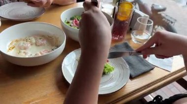 Yemek saatinde restorandaki ortak tabaktan salata alan bir kadının taze sebzeler ve modern sofra düzeniyle rahat bir yemek sahnesi oluşturması..