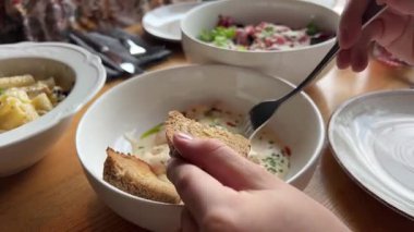Kadın ekmeğe karides koyup parmaklarıyla uyum sağlamak için çatal kullanırken aile yemeğinde kremalı sosu beyaz tabaklar ve taze yiyeceklerle birlikte ahşap masaya sürüyor..