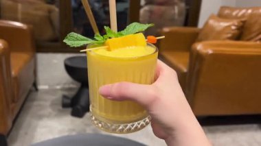 Bir bardak naneli mango smoothie. Arka planda yumuşak kahverengi deri koltuklar ve sıcak sıcak sıcak ışık görünüyor. Tropikal sakin bir hava yaratıyor..