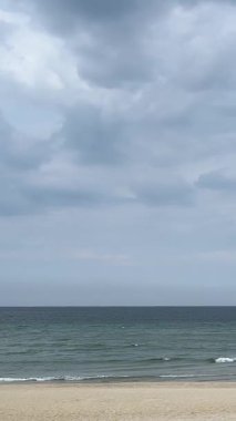 Phu Quoc Adası 'nda sakin kum, dalgalar ve palmiye yapraklarıyla huzurlu boş bir sahil. Gri bulutlar denizin üzerinde süzülürken uzak dağlar Vietnam ufkunda kayboluyor.. 