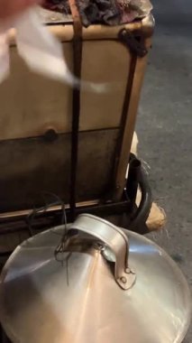 Vietnamlı bir sokak satıcısı motorsikletindeki çömlekten dumanı tüten bir banh bao kaldırıyor. Müşterilere sıcak çörekler sunarken buhar yükseliyor, otantik sokak yemeği kültürünü ve şehir hayatını yakalıyor.. 