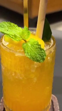 Elleri nazikçe mango bardağında saman karıştırıyor ve buzlu narenciye. Sıcak ışık, sıcak tropikal kafedeki cama yansıyor, tazeliği ve sakinliği çağrıştırıyor.. 