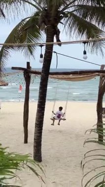 Phu Quoc Adası 'nda çocukların palmiye ağaçlarının altında sallanmaktan hoşlandıkları tropik bir plaj. Hamaklar rüzgarda sallanıyor, dalgalar okyanusta parıldıyor ve çok az insan cennette dinleniyor.. 