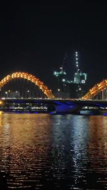 Da Nang Dragon Köprüsü 'nün parlak ışıklarıyla büyülü gece görüntüsü. İnsanlar ve arabalar Vietnam 'ın parlayan kalbinden geçerken yansımalar Han Nehri' nde dans ediyor.. 