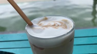 Kahve makinesine konmuş uzun bir bardakta kaymaklı buzlu kahve karıştırılıyor. Süt köpüğü hafifçe dökülüyor. Taze ev yapımı soğuk latte hazırlanıyor.. 