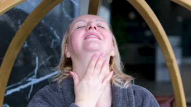 Bir kadın pencerenin kenarında otururken yüzüne ve boynuna masaj yapar. Duştan sonra bornozla banyo yaptıktan sonra. Yüksek kalite 4k görüntü