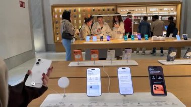 Genç kadınların canlı teknoloji alışveriş atmosferinin tadını çıkarırken tasarım ekranı ve kameradan bahseden akıllı telefonları karşılaştırıp seçtikleri Apple mağazasının içinde. Roma, İtalya 11.25.2025