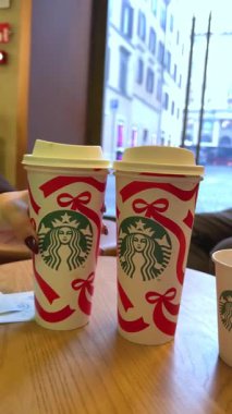 Kız elini uzatarak Starbucks 'ın yanında bir Noel temalı kağıt bardak makbuzu alıyor sıcak atmosfer keyfi ve yaşam tarzı detaylarıyla dolu mevsimlik sıcak bir kahve anı yaratıyor. Roma, İtalya 11.25.2025