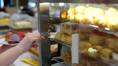 Müşteri fırında eldiven kullanarak taze pişmiş çoklu tahıllı ekmek seçiyor. Modern bir marketin self-servis bölümünde cam arkasında gösterilen zanaatkar somunların çeşitliliği. Günlük taze kabuklu. .