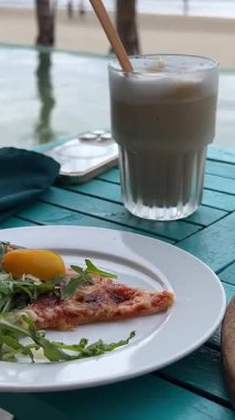 Plajda, buzlu lattenin yanında çatal ve bıçakla pizza dilimi kesiyor. Yüksek kalite 4k görüntü