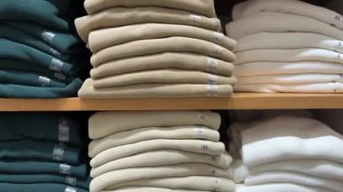 Bir mağaza rafında, açık mavi renkli ve görülebilir boyutta çıkartmalı temiz bir kazak yığını. Bu klip mevsimlik giyim koleksiyonları ve perakende organizasyonu için mükemmel..