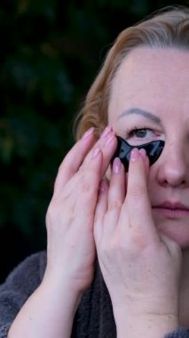 Gözlerinin altında yamalar olan güzel bir yetişkin kadın saçını düzleştiriyor. Yaşlanan cilde dikkat et. Bornozlu kadınlara siyah yamalar