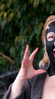 Omuz aynasından kendine bakan yüz maskeli genç bayanın yansıması ve daha iyi soğurmak için kuvars silindirli yüz masajı, cilt bakımı. siyah yüz maskesi