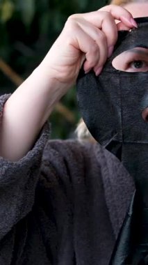 Omuz aynasından kendine bakan yüz maskeli genç bayanın yansıması ve daha iyi soğurmak için kuvars silindirli yüz masajı, cilt bakımı. siyah yüz maskesi