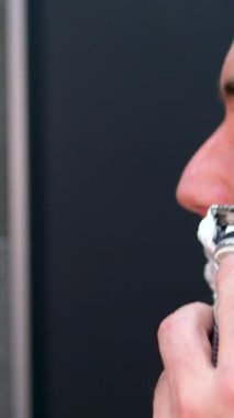 Sakalını elektrikli tıraş makinesi kullanarak tıraş eden bir adam. Erkek güzellik bakım konsepti. Banyo aynasına bakıp sakal kesen ev insanı..