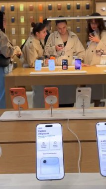 Genç kadınların canlı teknoloji alışveriş atmosferinin tadını çıkarırken tasarım ekranı ve kameradan bahseden akıllı telefonları karşılaştırıp seçtikleri Apple mağazasının içinde. Roma, İtalya 11.25.2025
