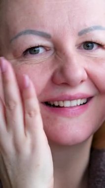 45 yaşlarında bir kadın krem masajı yapıyor. Alnı ve çenesi banyodan sonra yüz jimnastiği yapıyor. Kendine iyi baktığını ve cilt bakımını gösteriyor..