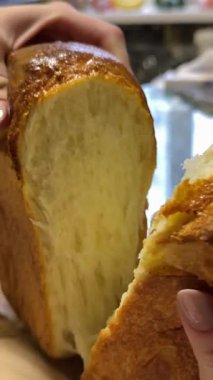 Yumuşak dokusunu ve altın kabuğunu gösteren taze pişmiş bir somun ekmeği parçalayan ellerin yakın çekimi. Ağır çekim. Yüksek kalite 4k görüntü