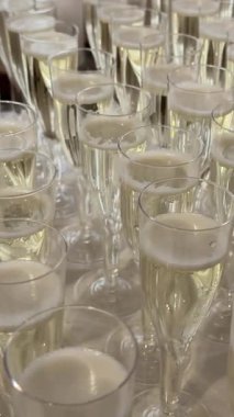 Sofistike bir etkinlikte kadehlerin içine zarif şampanya dökülüyor. Doldurulmuş, yemyeşil bir arka plan ve şenlikli bir atmosferi olan köpüklü şarap kadehlerinin detaylı bir görüntüsü..