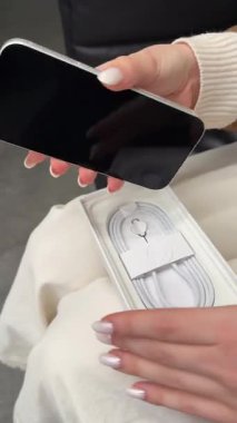 Kapalı Apple iPhone 17 Pro kutusu taşıyan kadın kazağı, rahat bir odada beyaz masada oturuyor. Ukrayna, Kyiv 12.12.2025