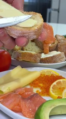 Yan manzara Şefi tereyağlı ekmeğin üzerine tuzlanmış somon dilimleri koyar ve sıcak mutfak ışıklarında açık sandviç yapar, 4K. Yemek blogları, yemek tarifi videoları ya da mutfak stokları için mükemmel..