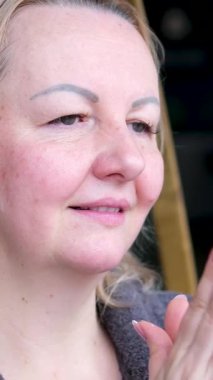 Olgun bir kadının daha önce temizlenmiş yüzüne nemlendirici krem sürerken ve mavi arka planda kameraya gülümserken güzel bir pozu. Cilt bakımı, kozmetik, sağlık hizmetleri kavramı.