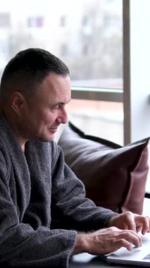 Evde çalışan dizüstü bilgisayar kullanan çekici bir adam. Yakışıklı erkek öğrenci, oturma odasındaki teknolojiyle çevrimiçi iletişim kurmak için bilgisayar defterine yazıp sohbet ediyor..