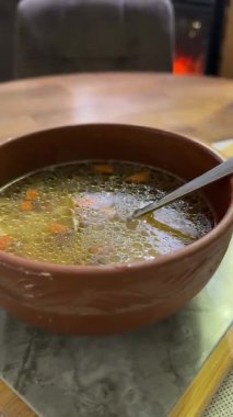 Sıcak sebze çorbası, kil kasede tavuk eti ve köy masasında servis ediliyor. Ön manzara, dikey olarak yaklaşırken. Küçük makarna.