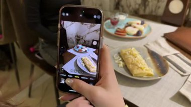 Bir kız yemeğinin fotoğrafını çeker: doldurulmuş lavaş, süzme peynirli krep ve bir restoranda süzme peynirli krep. Kızlar için iki porsiyon kahvaltı. Yüksek kalite 4k görüntü