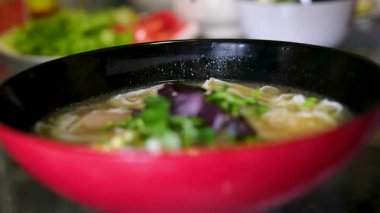 Erişte çorbasına fesleğen ekle. Masada kırmızı ve siyah çorba kasesi var. Yüksek kalite 4k görüntü