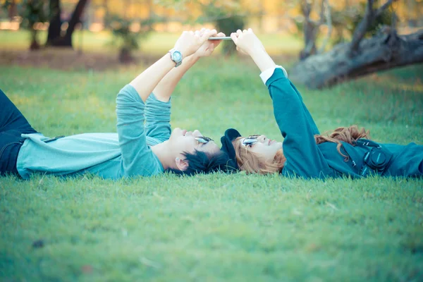 Casal deitado na grama, parque, telefone vista, cercado por nat — Fotografia de Stock