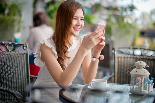 La Chica mensajes de texto en el teléfono inteligente en una terraza de restaurante con — Foto de Stock