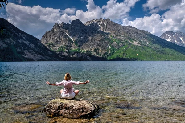 Jonge vrouw door meer en de bergen mediteren. — Stockfoto