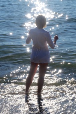 Kadın siluet ışıltılı su ile sahilde. 