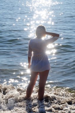 Kadın siluet ışıltılı su ile sahilde. 