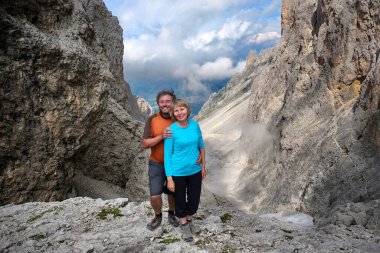Yüksek dağ geçidinde neşeli bir çift mutlu ve sağlıklı görünüyor. Orta yaşlı insanlar rüzgarlı dağlarda yürüyüş yapıyor. Dolomitler. İtalya. 
