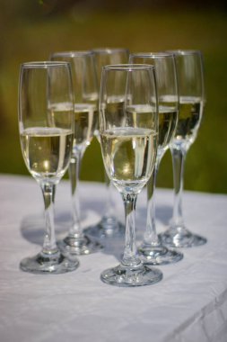 Beyaz bir masa örtüsü üzerinde köpüklü şarapla dolu şampanya bardaklarının yakın çekimi. Açık hava etkinliğinde kutlamaya hazır..