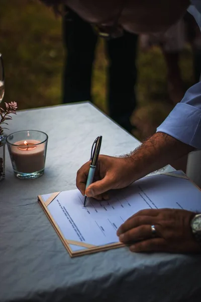 Açık hava seremonisi sırasında mum ve yumuşak doğal ışıkla romantik bir atmosfer yaratan bir adamın evlilik sertifikasını imzalarken..