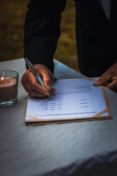 Resmi takım elbiseli bir adam açık hava seremonisi sırasında resmi bir düğün belgesi imzalıyor. Aşkı, birlikteliği ve ömür boyu bağlılığı simgeliyor..