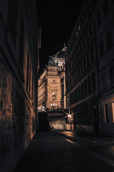 Prag 'daki aydınlatılmış Ulusal Tiyatro' ya doğru uzanan dar bir gece sokağı dramatik gölgeler, tarihi mimari ve karanlık çöktükten sonra bir Avrupa şehrinin atmosferik cazibesini vurguluyor..