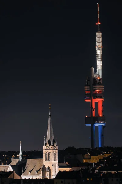 Prag 'ın çatısında yükselen ikov Televizyon Kulesi, dramatik bir gece sahnesindeki sıcak aydınlatmalı kilise kulesiyle çelişiyordu..