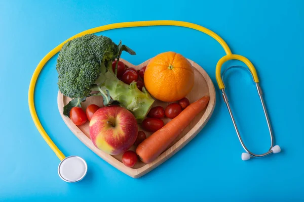 World diabetes day concept with clean fruits in nutritionist\'s heart dish. Yellow stethoscope on blue color background