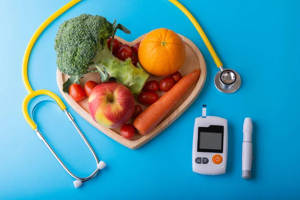 Diabetes monitor, diabetic measurement. World diabetes day concept with clean fruits in nutritionist\'s heart dish