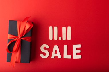 11.11 Bekar Günü indirimi. Kırmızı kurdeleli siyah hediye ve kırmızı arka planda ahşaptan yapılmış 11.11 satış metni. Üst görünüm