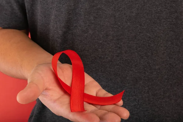 World AIDS day. Human hands holding red ribbon awareness on red background with copy space.