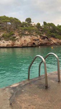 Mallorca, İspanya 'daki Cala Santanyi körfezinde turkuaz deniz suyuna çıkan metal havuz merdiveni. Kristal berraklığında dalgalanan su ve uçurumlara yakın