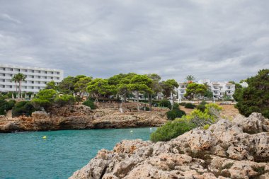İspanya 'nın Mallorca adasındaki Cala d' Or köyündeki Cala Esmeralda körfezi. İnsanlar denizin ötesindeki tepelerden kumsal manzarasının keyfini çıkarıyorlar..