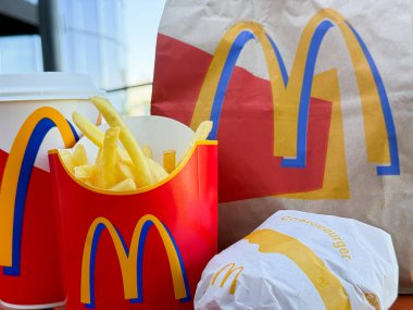 McDonald 's dışarıdaki teras masasının siparişi: markalı kağıt poşet, taze patates, hamburger ve içki.
