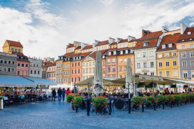 Varşova eski kasaba meydanı binaları, açık gökyüzü altındaki restoranlar ve turistler Polonya başkentini keşfetmek için zaman harcıyor